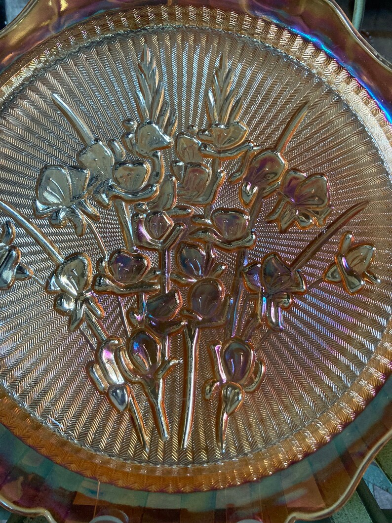 Peut inclure: Une assiette de service en verre iris&eacute; vintage avec un motif floral en relief. L'assiette a un bord festonn&eacute; et une surface textur&eacute;e.