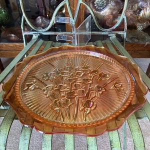 Peut inclure: Une grande assiette de service en verre ambr&eacute; avec un bord festonn&eacute;. L'assiette pr&eacute;sente un motif en relief d'un bouquet de fleurs.