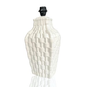 Op de afbeelding: Een witte keramische tafellamp met een gevlochten mandontwerp. De lamp heeft een zwarte lamphouder en een lampvoet. De lamp is een decoratief item voor in huis.