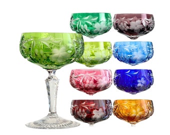 May include: Set of eight stemmed crystal glasses with intricate etched floral designs. The glasses are in various colors, including green, blue, red, and amber.