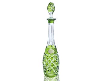 May include: A tall, elegant green glass decanter with a matching stopper. The decanter features a diamond-cut pattern on the base and a slender, ribbed neck. The stopper has a decorative, faceted design. The decanter is likely used for serving beverages.