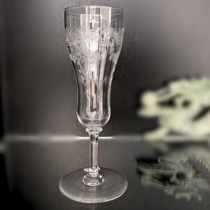 Può includere: Un flauto da champagne in vetro trasparente con un motivo floreale inciso. Il flauto ha un gambo lungo e una coppa larga.