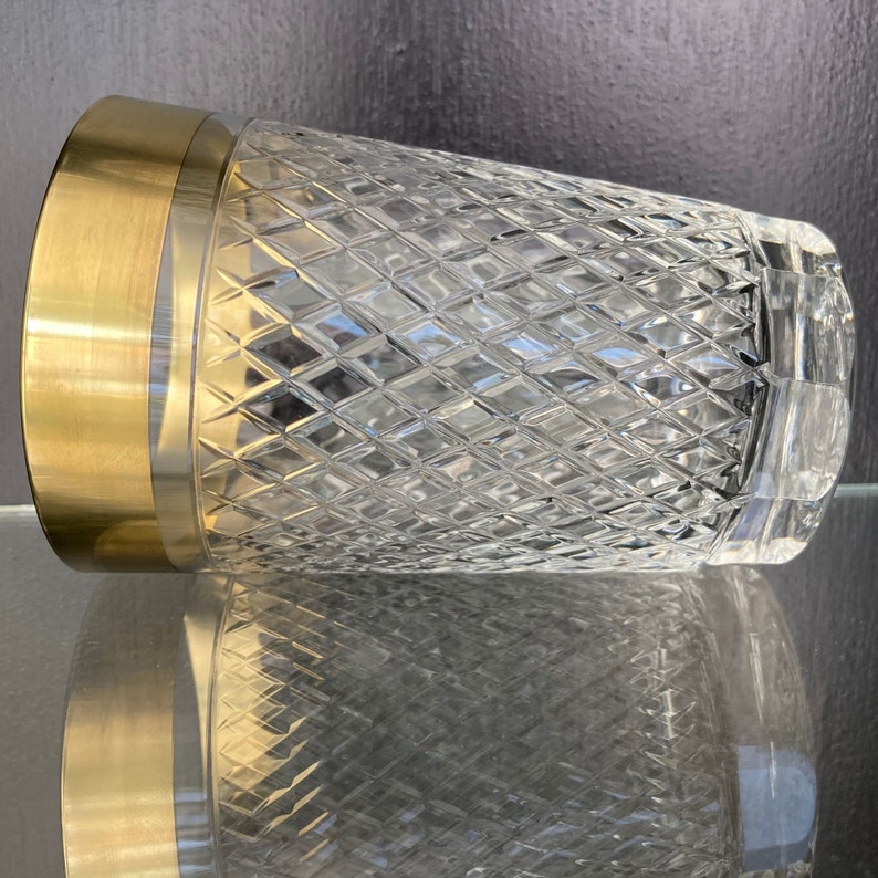 May include: A clear glass vase with a gold rim and a diamond pattern. The vase is sitting on a reflective surface.