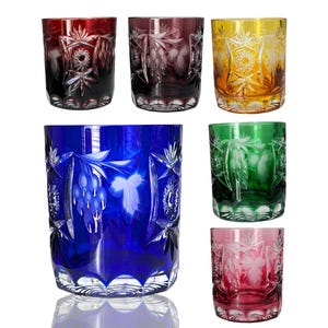 Könnte beinhalten: Sechs farbige Trinkgläser aus geschliffenem Glas. Die Gläser sind in Rot, Lila, Gelb, Blau, Grün und Rosa gehalten. Jedes Glas hat ein detailliertes Blumen- und Sternmuster, ideal für Getränke.