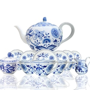 Può includere: Un set da tè in porcellana blu e bianca con una teiera, una lattiera, una zuccheriera e sei tazze e piattini. Il set presenta un motivo floreale con fiori e foglie blu su sfondo bianco.