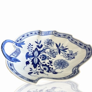 Peut inclure: Un plat de service en porcelaine blanche avec un motif floral bleu et une poignée. Le plat a un bord festonné et est décoré d'un motif floral bleu et blanc.