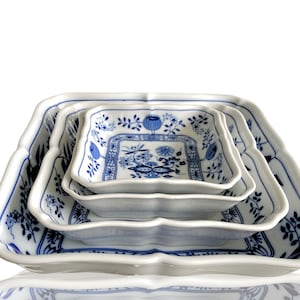 May include: Set of three white porcelain square serving dishes with blue floral designs. The dishes are nested inside each other.