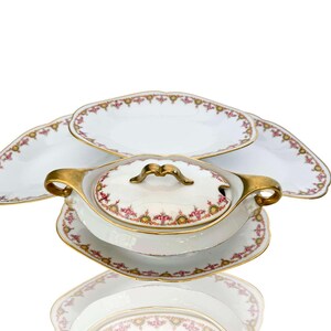 Op de afbeelding: Een witte porseleinen serveerset met gouden rand en roze bloemmotieven. De set bevat een grote ovale schaal, twee kleinere ovale schalen, een ronde kom met deksel en een kleinere ronde schotel.