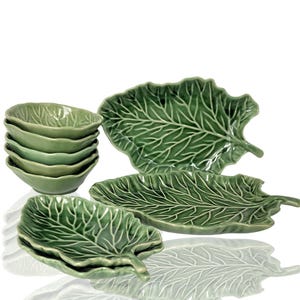 Peut inclure: Ensemble de bols et d'assiettes en céramique verte en forme de feuilles de chou. Les bols sont empilés et les assiettes sont disposées en éventail.
