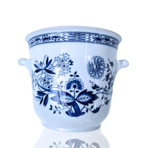 Peut inclure: Un pot en céramique blanche avec des motifs floraux bleus et deux poignées. Le pot a une bordure bleue et blanche autour du haut.