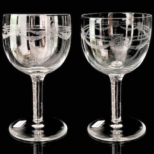 Op de afbeelding: Twee heldere glazen wijnglazen met gegraveerde ontwerpen. De glazen hebben een ronde kom en een lange, dunne steel.