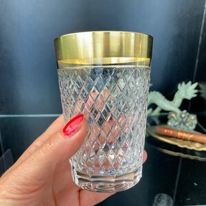 May include: A clear glass tumbler with a gold rim and a diamond-shaped pattern. The glass is held in a hand.
