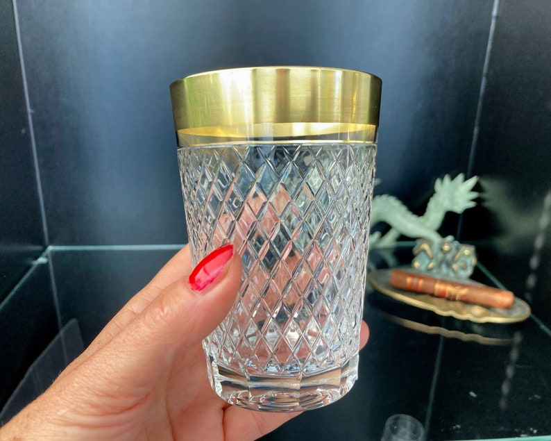 May include: A clear glass tumbler with a gold rim and a diamond-shaped pattern. The glass is held in a hand.