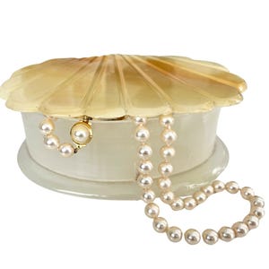 May include: A white alabaster shell-shaped trinket box with a gold-colored lid and a pearl necklace inside.
