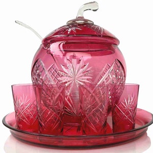 Op de afbeelding: Een set van robijnrode glazen punchkom en bekers met een geslepen glasontwerp. De set bevat een kom met deksel, een lepel en vier bekers. De kom en bekers staan op een bijpassend dienblad.