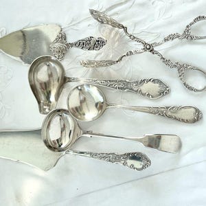 Könnte beinhalten: Ein Set aus fünf silbernen Servierstücken, darunter ein Kuchenspachtel, eine Schöpfkelle, ein Löffel, eine kleinere Schöpfkelle und eine Zange. Die Stücke sind alle mit floralen Mustern verziert.