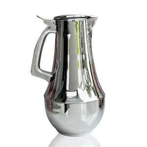May include: A polished, silver-coloured jug with a curved body and a large handle. The jug has a hinged lid and a spout for pouring. The reflective surface of the jug creates a mirror-like effect, reflecting the surrounding environment.