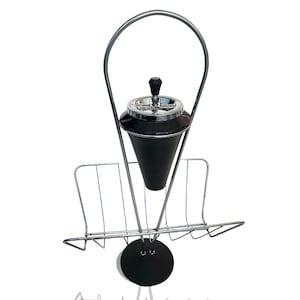 May include: A vintage chrome and black ashtray stand with a magazine rack. The ashtray is cone-shaped and has a silver rim. The stand has a circular base and a curved handle. The magazine rack is made of wire.