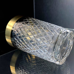 May include: A clear glass tumbler with a gold rim and a diamond pattern. The glass is empty and is sitting on a black surface.