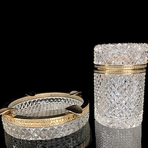 Pode incluir: Um conjunto de dois cinzeiros de cristal vintage com acabamento dourado. Ambos os cinzeiros são redondos e têm um padrão de diamante. O cinzeiro maior tem uma tampa.