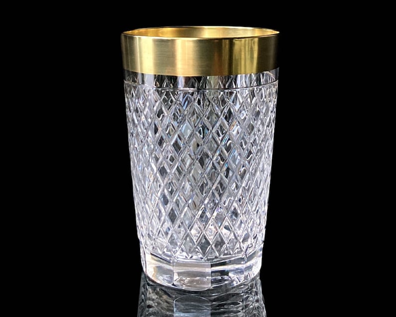 May include: A clear glass tumbler with a gold rim and a diamond pattern. The tumbler is on a black background.