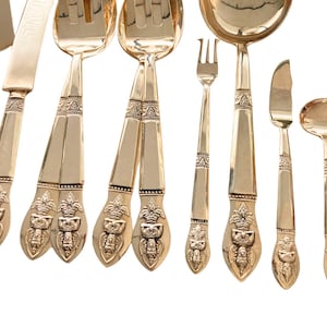 Op de afbeelding: Een set van verguld bestek met sierlijke handvatten. De set bevat een serveerschep, een serveervork, een botermes, een taartschep, een soeplepel, een diner vork en een theelepel.