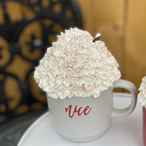 May include: White ceramic mug with a whipped cream topping and a sprinkle of cocoa powder. The mug has the word "nice" written on it in red.