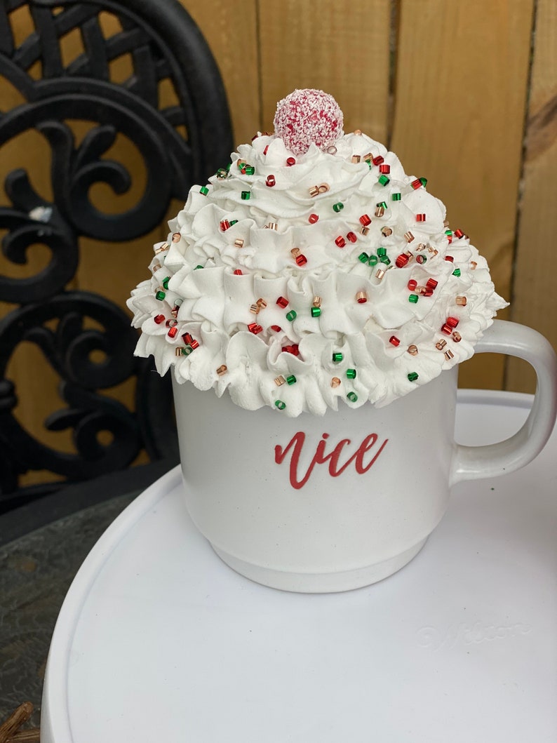 May include: White ceramic mug with a red and green sprinkle topping and a red cherry on top. The mug says "nice" in red lettering.
