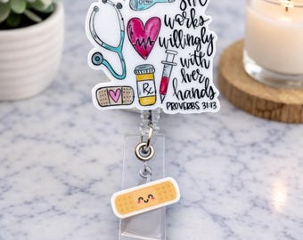 May include: A white badge reel with a medical theme. It features a stethoscope, heart, thermometer, pill bottle, syringe, and a bandage with a heart. The text reads "She works willingly with her hands" and "Proverbs 31:13".