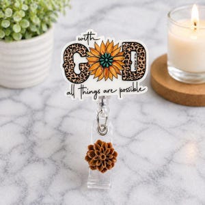 May include: A white badge reel with the words "with GOD all things are possible" and a sunflower design. The letters "G" and "D" have a leopard print pattern. The reel has a brown flower accent.