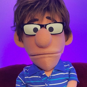 May include: A blue and white striped polo shirt with a brown puppet head wearing black framed glasses. The puppet is sitting on a red chair with a white tag that says "Maker Data Makers".
