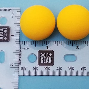 May include: Two bright yellow foam balls, each about 1 inch in diameter, are shown next to a ruler.