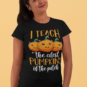 Peut inclure: T-shirt noir avec un graphique de trois citrouilles orange avec des visages et le texte "J'enseigne les citrouilles les plus mignonnes du champ".