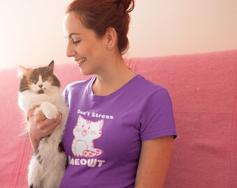 May include: A purple t-shirt with the text "Don't Stress MEOWT" and a cartoon cat graphic. A person is holding a calico cat with white, brown, and black fur. The cat is looking at the camera.