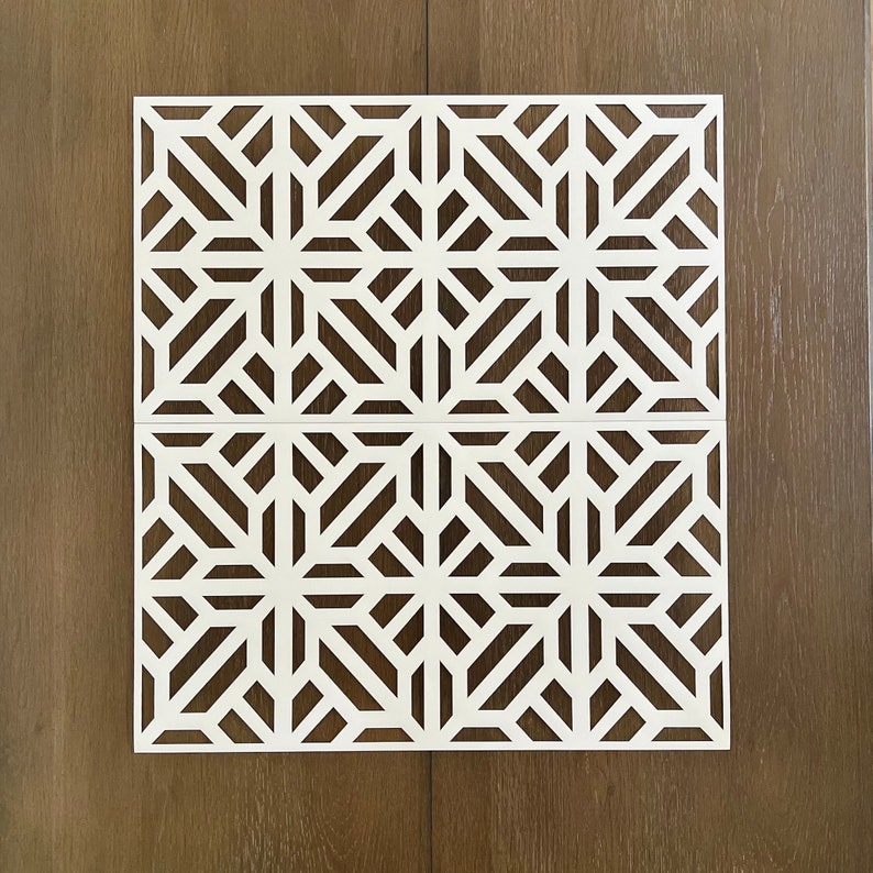 May include: White geometric stencil with a repeating pattern of intersecting lines creating a starburst design. The stencil is on a brown wood background.