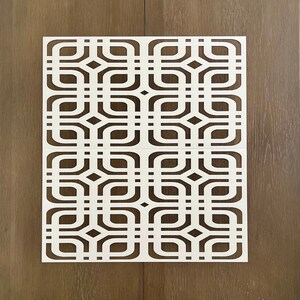 May include: White geometric stencil with a repeating pattern of squares and rounded shapes. The stencil is made of a thin, flexible material and is designed for use with paint or other mediums.