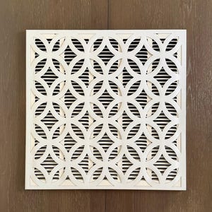 May include: A square white air vent cover featuring a repeating geometric pattern of interlocking circles. The decorative front panel is layered over a series of horizontal slats, creating a high-contrast design that allows for airflow.