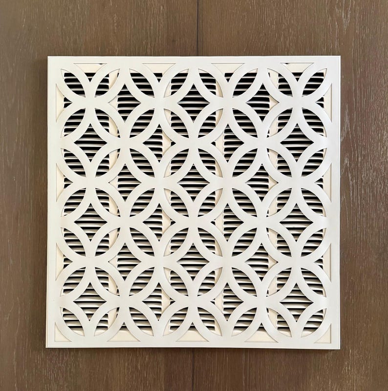 May include: A square white air vent cover featuring a repeating geometric pattern of interlocking circles. The decorative front panel is layered over a series of horizontal slats, creating a high-contrast design that allows for airflow.