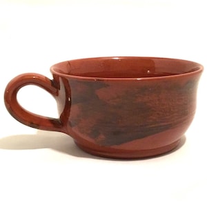 May include: A brown ceramic mug with a wide, rounded shape and a handle. The mug has a mottled brown glaze with darker brown streaks.