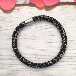May include: A black and silver beaded necklace with a geometric pattern. The necklace has a magnetic clasp.
