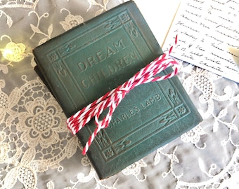 Pode incluir: Um pequeno livro de capa dura verde-escuro intitulado Dream Children de Charles Lamb, envolto em barbante vermelho e branco. A capa apresenta bordas decorativas e letras em relevo, amarrado com um laço centralizado.