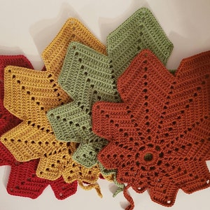 May include: A collection of handmade crochet leaf-shaped trivets in fall colors: red, gold, olive green, and rust. Each trivet features a detailed openwork design and a small loop for hanging. These trivets are perfect for protecting surfaces from hot dishes.