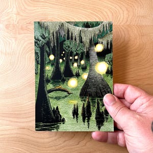 May include: A black and white illustration of a swamp with tall trees and glowing orbs of light. The trees have moss hanging from their branches and the water is a dark green color.