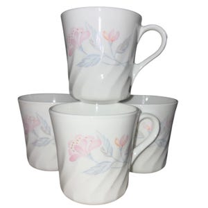 May include: A set of four white ceramic mugs. Each mug features a floral design with pink flowers, light blue leaves, and orange accents. The mugs have a curved handle and a textured, ridged pattern.