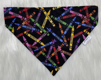 May include: Black bandana with a pattern of colorful crayons with the words 'Red', 'Yellow', 'Blue', 'Green', 'Orange', 'Purple', and 'Pink' written on them. The bandana has a tag that says 'Simba's Creations'.