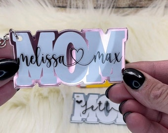 May include: A pink and white acrylic keychain with the word "MOM" in large letters. The names "melissa" and "max" are written in cursive script on either side of the heart.