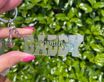 May include: A clear acrylic keychain with the word "Daddy" in silver glitter lettering. The word "family" is written in cursive above the word "Daddy". A silver axe charm is attached to the keychain.