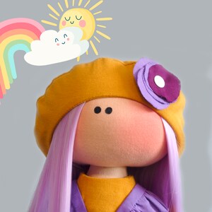 May include: A handmade doll with purple hair, a yellow beret with a purple flower, and a yellow dress. The doll is smiling and has a happy expression. The background is a light gray with a rainbow and a sun.