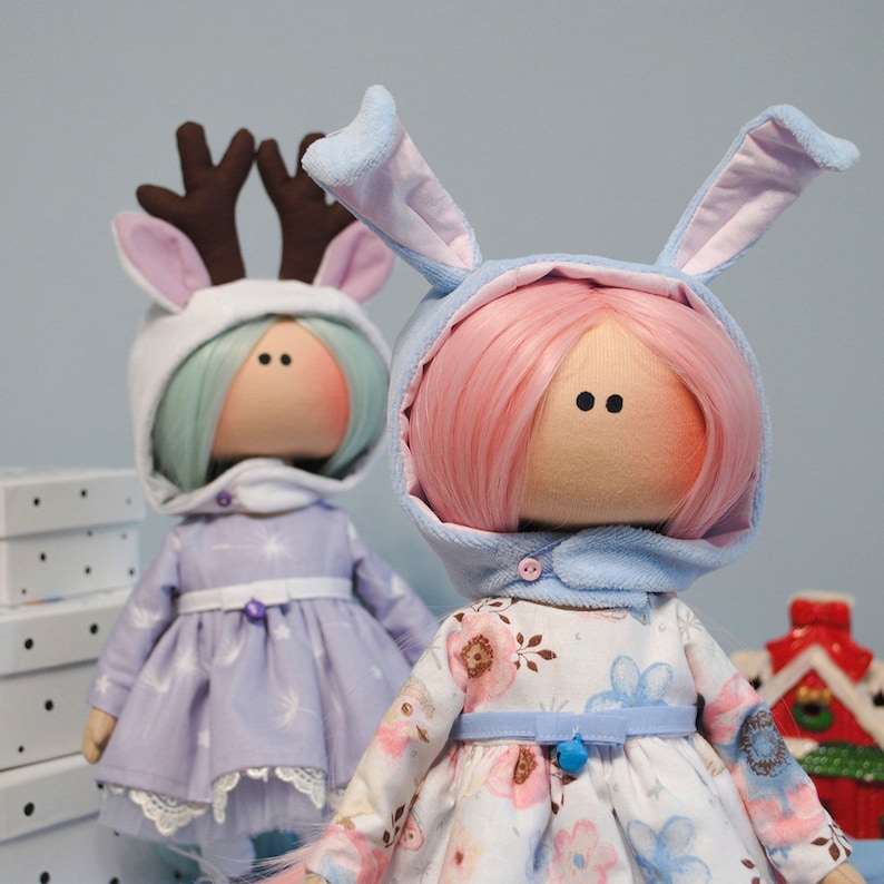 May include: Two handmade fabric dolls wearing winter-themed outfits. One doll has pink hair and a blue bunny costume, the other has green hair and a white reindeer costume.