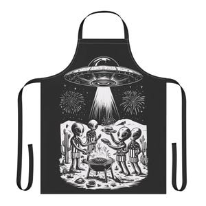 Puede incluir: Delantal negro con una ilustración en blanco y negro de extraterrestres haciendo una barbacoa. Un OVNI flota sobre los extraterrestres, con fuegos artificiales en el fondo. Los extraterrestres se reúnen alrededor de una parrilla.